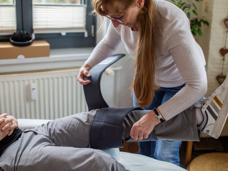 Heidi Siegertlegt eine graue Manschette um das Bein eines liegenden Klienten für eine Anwendung mit Bemer in Bautzen.