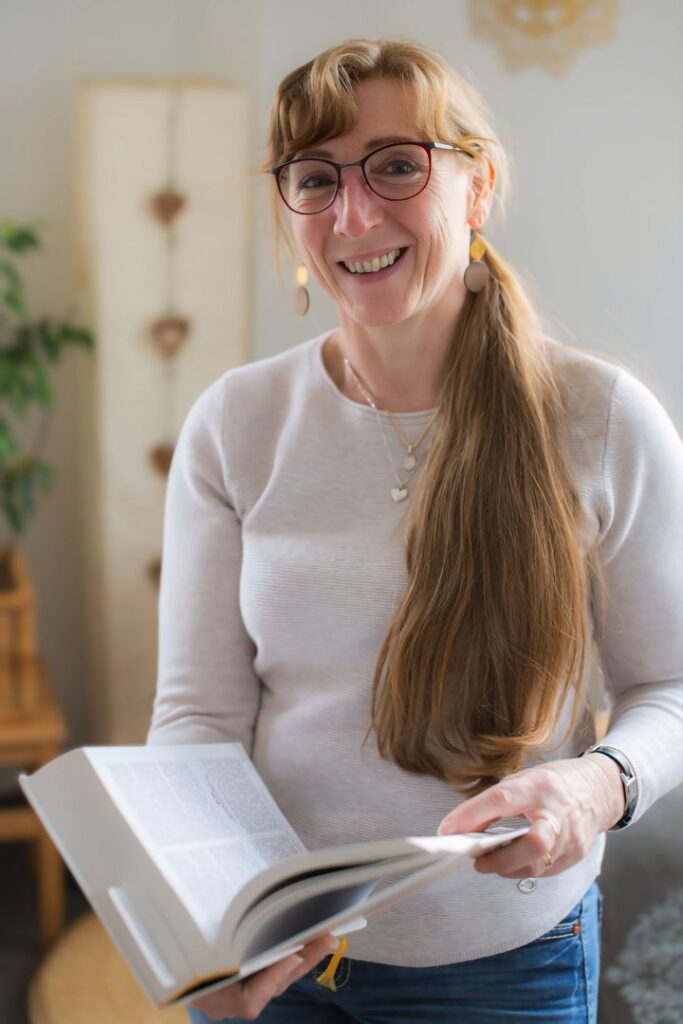 Heidi Siegert mit Brille hält ein dickes und aufgeschlagenes Fachbuch in den Händen als Symbol für die Burnout Prävention Bautzen.