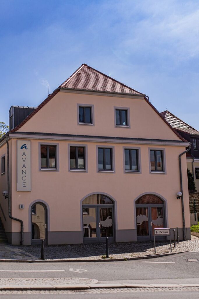 Die Außenansicht eines pfirsichfarbenen Gebäudes mit großen Bogenfenstern und dem Praxisschild, dem Standort für Energiearbeit in Bautzen.