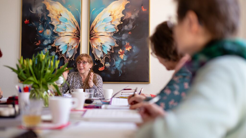 Heidi Siegert leitet ein Seminar zum Thema Energiearbeit in Bautzen. Man sieht viele Teilnehmer und im Hintergrund ein Bild mit einem riesigen bunten Schmetterling.