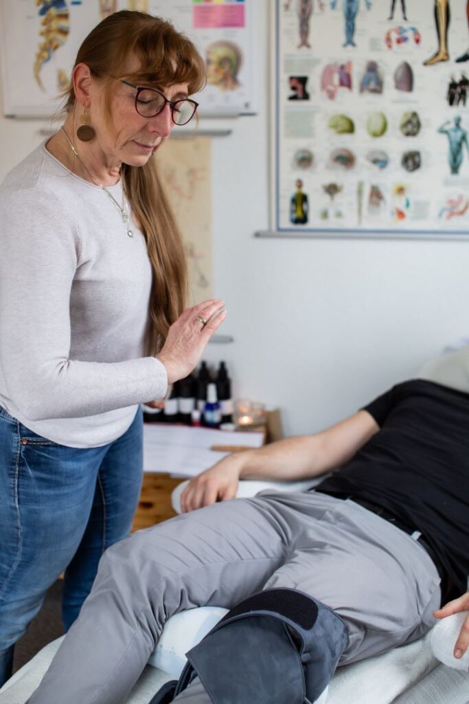 Heidi Siegert hält ihre flache Hand mit Abstand über den Körper eines liegenden Mannes um das energetische Narbenentstören durchzuführen.