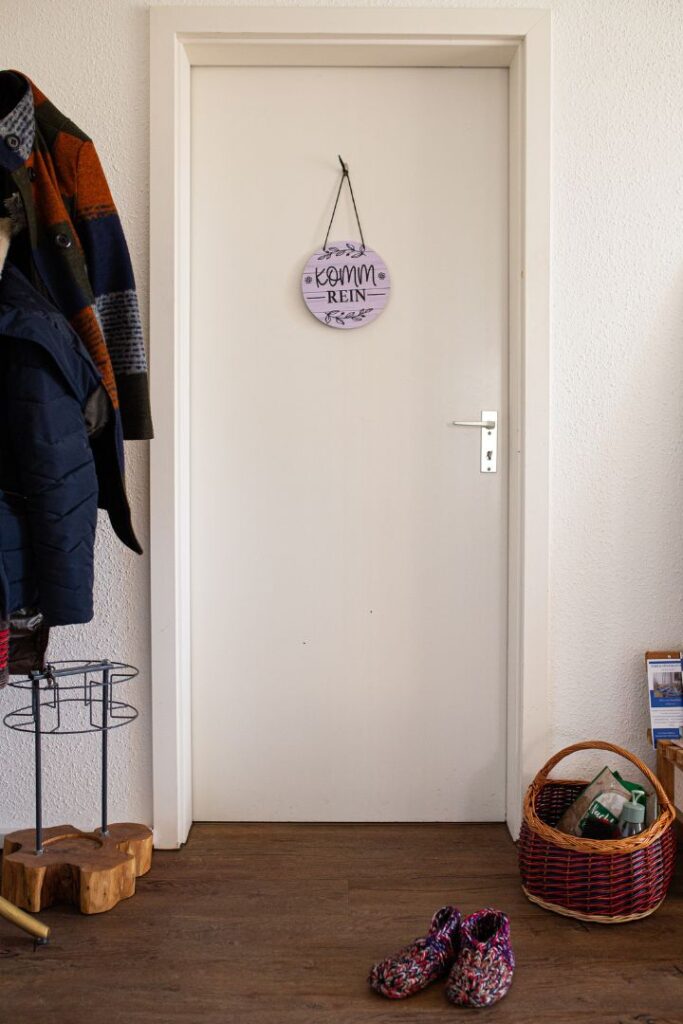 Eine weiße Praxistür mit einem runden Schild mit der Aufschrift Komm REIN und davorstehenden Hausschuhen lädt Klienten mit dem Thema Schlafprobleme in Bautzen ein.
